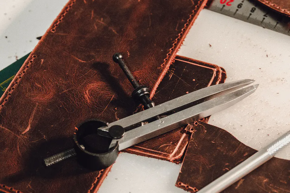 Peças de couro, uma régua de metal e um compasso de pontas na bancada de um artesão de couro